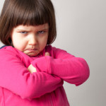 frustrated young child sulking with crossed arms and dirty look